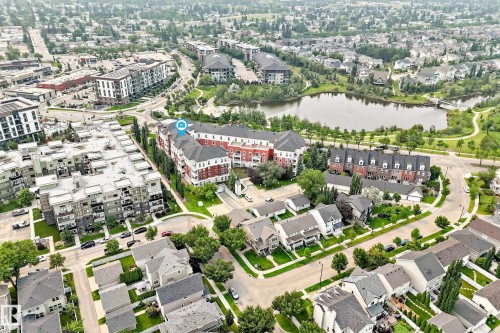 Aerial view showcasing the building's facade, multiple apartment buildings, single-family homes, and a prominent lake with surrounding green space - #307 1003 Gault Bv Nw, Edmonton, AB -  With View