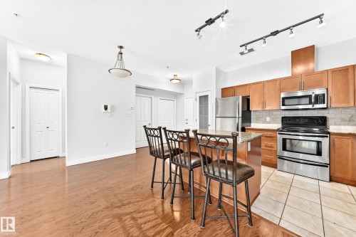 Open-concept kitchen featuring wood cabinetry, stainless steel appliances, and a tiled backsplash - #307 1003 Gault Bv Nw, Edmonton, AB - Indoor Photo Showing Kitchen