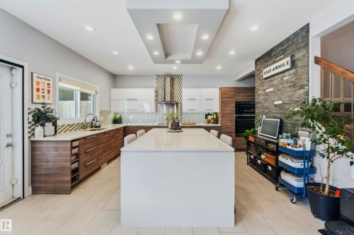 Modern kitchen featuring a large center island, wood-finish lower cabinetry, white upper cabinetry, and a textured tile backsplash - 7 Etoile Cres, St. Albert, AB 
