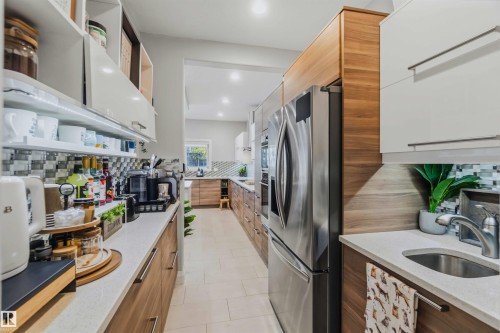 Galley kitchen featuring stainless steel appliances, wood-finish cabinetry, white upper cabinets, light-toned countertops, and a tiled backsplash - 7 Etoile Cres, St. Albert, AB 