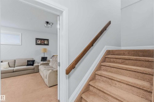 Carpeted stairs with a wood handrail, leading to a room featuring light-colored walls and a fixed ceiling-mounted projector - 7 Etoile Cres, St. Albert, AB 