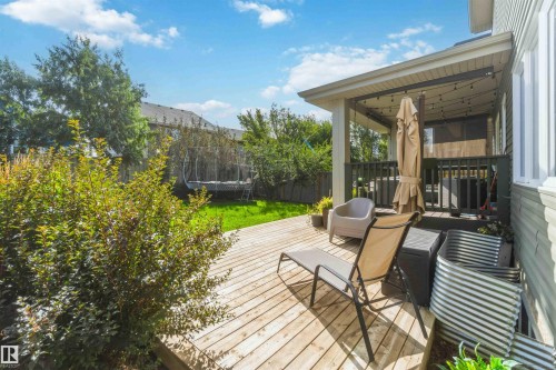 Expansive wood deck with a covered porch featuring string lights, overlooking a manicured lawn and mature landscaping - 7 Etoile Cres, St. Albert, AB 