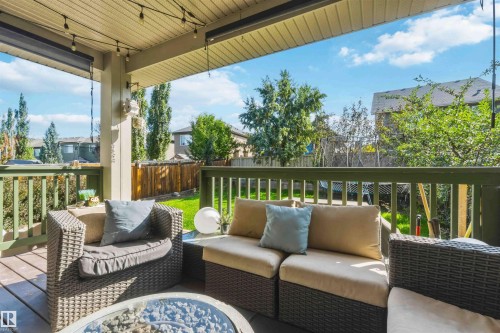 Covered outdoor deck with string lighting, wood-finish flooring, and green railings overlooking a fenced backyard with a lawn - 7 Etoile Cres, St. Albert, AB 
