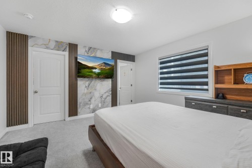 Wall-mounted television with marble-patterned accent wall, wood-finish slat details, and light gray carpeting - 12843 67 Street Nw, Edmonton, AB 