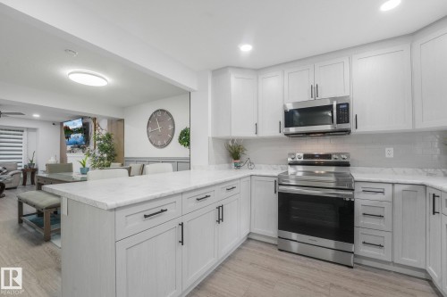 Modern kitchen featuring white shaker cabinetry, stainless steel appliances, stone countertops, and wood-finish flooring - 12843 67 Street Nw, Edmonton, AB 