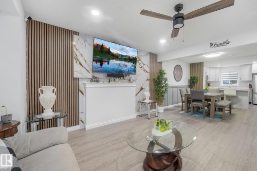 Wood-finish flooring throughout the open-concept living area, featuring a decorative slatted wall panel and a ceiling fan with integrated lighting - 12843 67 Street Nw, Edmonton, AB 