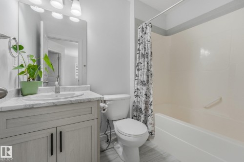 Bathroom featuring a vanity with a white countertop and undermount sink, a toilet, a shower-over-tub combination, and light wood-finish flooring - 12843 67 Street Nw, Edmonton, AB 