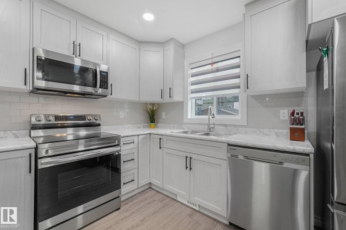 Light gray cabinetry with matte black hardware, stainless steel appliances, marble-look countertops, and white subway tile backsplash - 12843 67 Street Nw, Edmonton, AB 