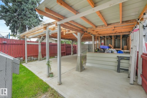 Covered patio area with concrete flooring, red wood fence, and partial grassy area - 12843 67 Street Nw, Edmonton, AB 