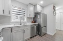 Kitchen featuring white shaker-style cabinetry, stainless steel appliances, a double basin sink with a gooseneck faucet, light-toned countertops, and wood-finish flooring - 12843 67 Street Nw, Edmonton, AB 