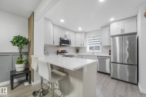 Kitchen featuring light-toned cabinetry, stainless steel appliances, a white stone-finish countertop, and wood-finish flooring - 12843 67 Street Nw, Edmonton, AB 