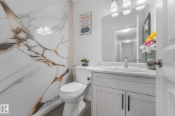 Vanity with a white countertop and integrated sink, under-sink cabinetry with black hardware, wall-mounted mirror, and a wall panel with gold-toned veining - 