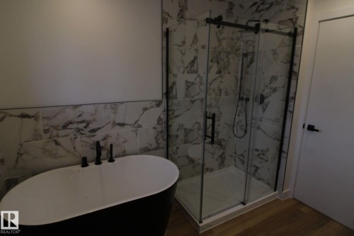 Freestanding soaking tub with matte black fixtures, glass-enclosed shower with matte black hardware, and floor-to-ceiling tile surround - 4224 110 Street Nw, Edmonton, AB 