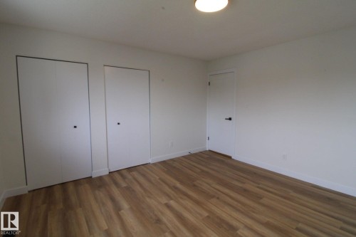 Wood-finish flooring, white walls, two bi-fold closet doors, and a flush mount ceiling light - 4224 110 Street Nw, Edmonton, AB 
