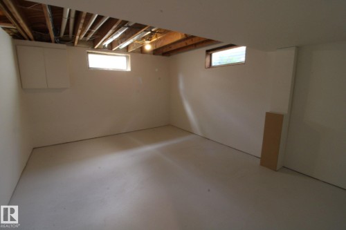 Unfinished basement with exposed ceiling joists, concrete flooring, and two transom windows - 4224 110 Street Nw, Edmonton, AB 