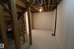 Unfinished basement space with exposed wood framing, white painted walls, and light-colored concrete flooring - 