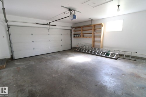 Attached garage with a white sectional door, integrated garage door opener, concrete flooring, and built-in shelving - 4224 110 Street Nw, Edmonton, AB 