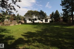 Expansive grassy backyard featuring mature trees, a wooden privacy fence, and multiple raised garden beds - 