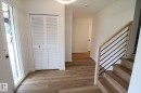 Wood-finish flooring throughout, white louvered bifold closet doors, and a staircase with light wood banister and black metal spindles - 4224 110 Street Nw, Edmonton, AB 