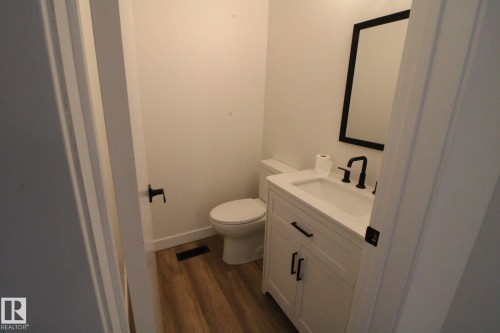 White vanity with an integrated sink, matte black faucet, framed mirror, and wood-finish flooring - 4224 110 Street Nw, Edmonton, AB 
