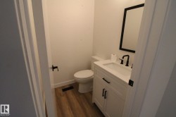 White vanity with an integrated sink, matte black faucet, framed mirror, and wood-finish flooring - 