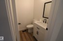 White vanity with an integrated sink, matte black faucet, framed mirror, and wood-finish flooring - 4224 110 Street Nw, Edmonton, AB 