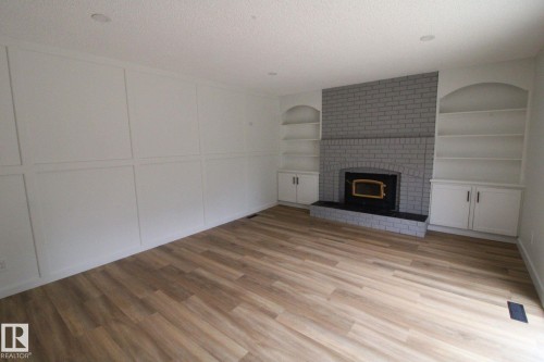 Wood-finish flooring, accent wall with paneling, brick-surround fireplace with hearth, and built-in shelving with cabinetry - 4224 110 Street Nw, Edmonton, AB 