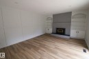 Wood-finish flooring, accent wall with paneling, brick-surround fireplace with hearth, and built-in shelving with cabinetry - 4224 110 Street Nw, Edmonton, AB 