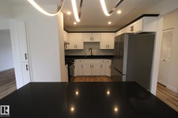 Modern kitchen featuring white cabinetry, dark countertops, recessed lighting, and wood-finish flooring - 