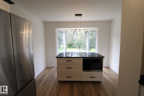 Kitchen featuring a central island with a dark countertop and white cabinetry, wood-finish flooring, a stainless steel refrigerator, and a bay window - 4224 110 Street Nw, Edmonton, AB 