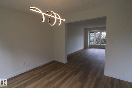 Open-concept interior featuring wood-finish flooring, a contemporary spiral chandelier, and a large window - 4224 110 Street Nw, Edmonton, AB 