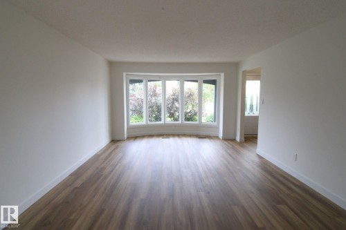 Spacious interior with neutral white walls, wood-finish flooring, and a curved bay window - 4224 110 Street Nw, Edmonton, AB 