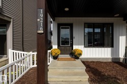 Modern exterior featuring vertical white siding, horizontal brown siding, a dark brown entry door with glass insert, black-framed windows, and concrete steps - 
