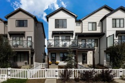 Modern townhome exterior with vertical siding, black-framed windows, and a white picket fence - 