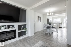 Built-in media console with an electric fireplace, wood-finish flooring, recessed shelving, and a modern chandelier - 