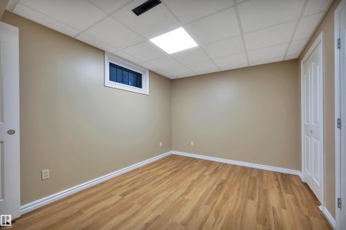 Wood-finish flooring, drop ceiling with integrated lighting, window with security bars, bi-fold closet doors, and neutral wall paint - 13416 102 Street Nw, Edmonton, AB 