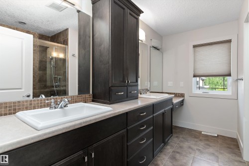 Dual vanity with integrated sinks, dark wood-finish cabinetry, a tall storage cabinet, and a tiled shower enclosure - 17535 110 Street Nw, Edmonton, AB 