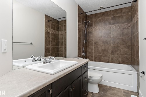 Tiled shower surround with decorative mosaic accent, white bathtub, dark wood-finish vanity, integrated sink, and full-width mirror - 17535 110 Street Nw, Edmonton, AB 