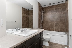 Tiled shower surround with decorative mosaic accent, white bathtub, dark wood-finish vanity, integrated sink, and full-width mirror - 