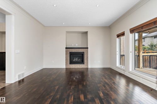 Dark-tone wood flooring, recessed lighting, crown molding, integrated fireplace with stone tile surround, and outdoor deck access - 17535 110 Street Nw, Edmonton, AB 