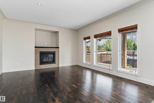 Dark wood-finish flooring, recessed lighting, crown molding, built-in fireplace with a stone surround and mantel, and multiple windows with wood blinds - 17535 110 Street Nw, Edmonton, AB 