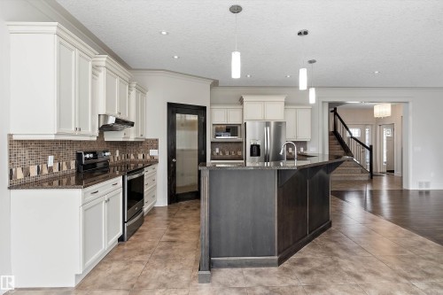 Kitchen featuring white cabinetry, dark countertops, mosaic tile backsplash, a center island with pendant lighting, and stainless steel appliances - 17535 110 Street Nw, Edmonton, AB 