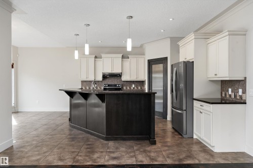 Spacious kitchen featuring an angular island with a dark wood finish, light-toned upper and lower cabinetry, stainless steel appliances, and tile flooring - 17535 110 Street Nw, Edmonton, AB 