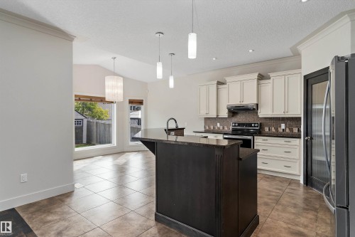 Kitchen featuring an island with a dark finish, light-toned cabinetry, tile flooring, recessed lighting, and a vaulted ceiling - 17535 110 Street Nw, Edmonton, AB 
