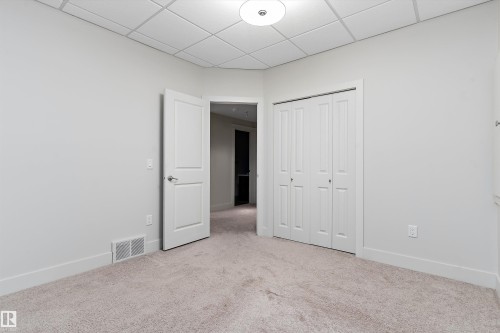 Neutral tone wall paint, light-colored carpet, white interior door, bi-fold closet doors, and recessed grid ceiling - 17535 110 Street Nw, Edmonton, AB 