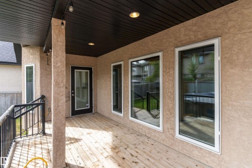 Covered outdoor deck with wood-finish flooring, stucco exterior, and black metal railings - 17535 110 Street Nw, Edmonton, AB 