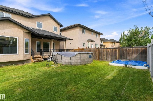 Spacious backyard featuring a covered deck with railing, an above-ground pool, a wooden fence, and a manicured lawn - 17535 110 Street Nw, Edmonton, AB 