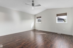 Vaulted ceiling, wood-finish flooring, two windows, ceiling fan with light, and neutral wall tones - 