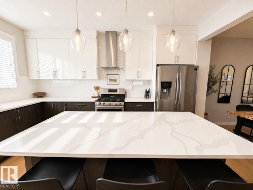 Kitchen featuring a large central island with a stone countertop, stainless steel appliances, white subway tile backsplash, and overhead pendant lighting - 10516 76 Street Nw, Edmonton, AB 
