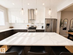 Kitchen featuring a large central island with a stone countertop, stainless steel appliances, white subway tile backsplash, and overhead pendant lighting - 